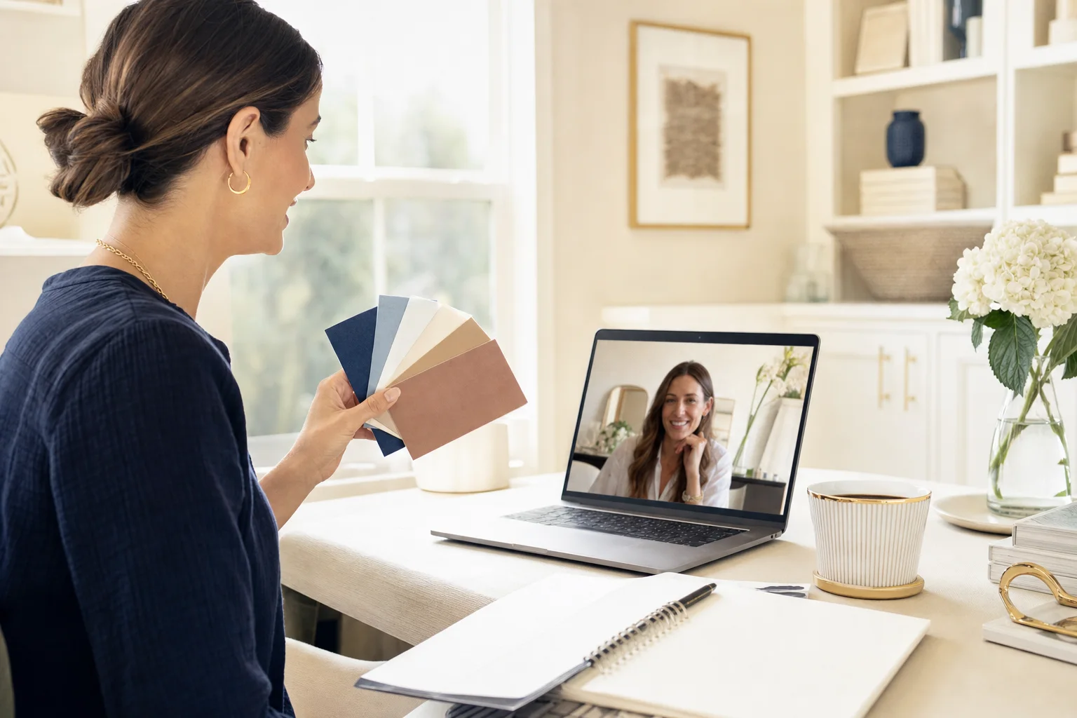 A stylist on a video call holds a fan of color swatches up to her laptop camera